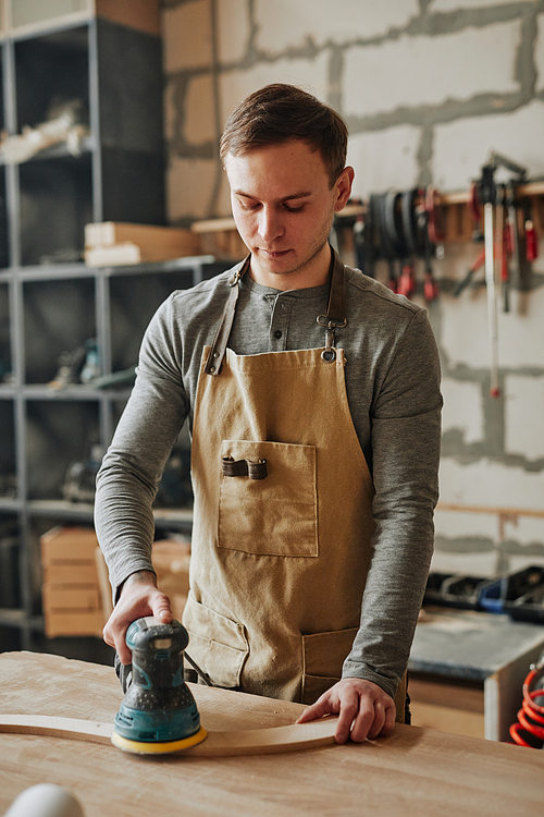 Vertical portrait of carpenters apprentice sanding wood while building handcrafted furniture in workshop