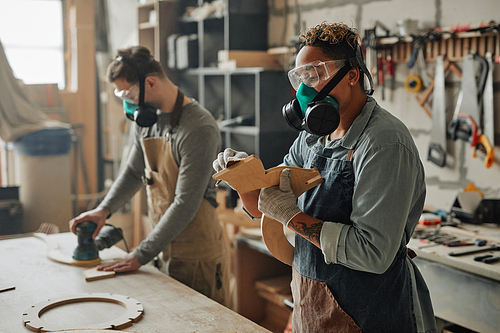 Side view portrait of two carpenters in protective gear working with wood while building handicraft furniture in workshop