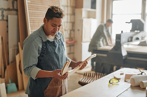 Warm toned portrait of female carpenter inspecting wooden furniture parts in sunlit workshop, copy space