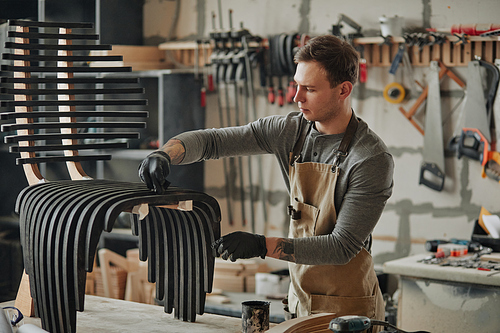 Warm toned portrait of young carpenter building designer wooden furniture in workshop, copy space