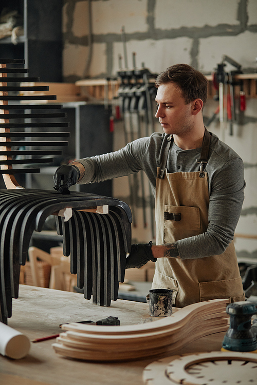 Vertical portrait of young carpenter building designer wooden furniture in workshop