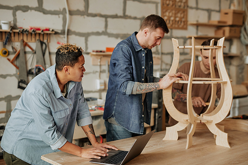 Warm toned portrait of two modern carpenters designing wooden furniture in workshop interior