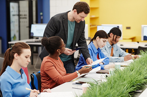 Vibrant portrait of male teacher helping diverse group of students in college during lab work