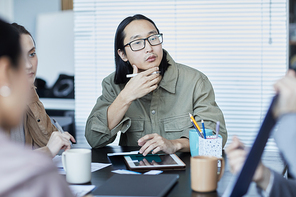 Portrait of pensive Asian man in business meeting with group of people discussing project in office