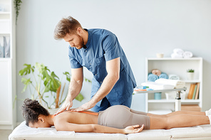 Portrait of rehabilitation specialist putting physio tape on back of young woman lying on massage bed