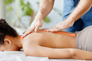 Closeup of rehabilitation specialist putting physio tape on back of young woman, copy space