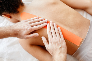 Top view of male rehabilitation therapist putting physio tape on back of young woman, copy space