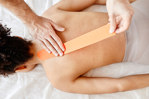 Top down view of rehabilitation therapist putting physio tape on back of young woman, copy space