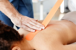 Close up of male rehabilitation therapist putting physio tape on back of young woman lying down, copy space