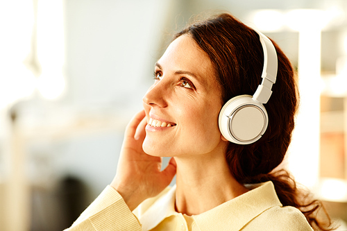 Close-up of charming young adult Caucasian woman wearing wireless headphones enjoying perfect sound of favourite music