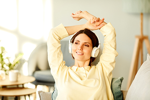 Young adult Caucasian woman wearing casual clothes relaxing in living room at home listening to music looking away