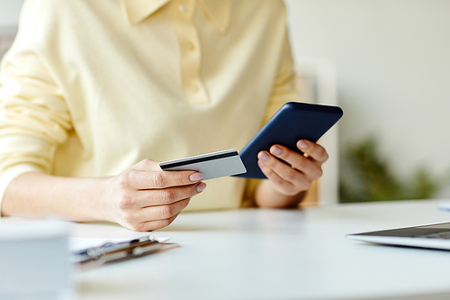 Unrecognizable woman sitting at desk ordering meal delivery or buying items online using app on smartphone and bank card