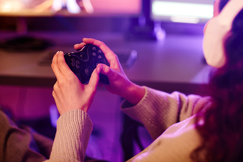 Unrecognizable woman wearing headphones holding controller having fun in evening playing video games