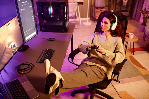 High angle view of young adult Caucasian woman playing shooter video game using console in living room at night