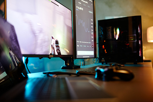 Horizontal no people shot of laptop, computer and video game console controller on table in room belonging to gamer and cryptocurrency trader