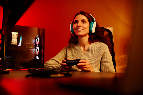 Modern young adult Caucasian woman playing racing or shooter video game using console in living room at night