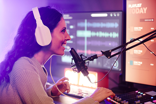 Modern young adult Caucasian woman wearing headphones recording podcast or broadcast using microphone, mixer and computer