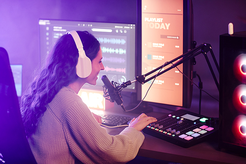 Young woman with long curly hair wearing headphones working in amateur radio station telling stories and turning on music for listeners