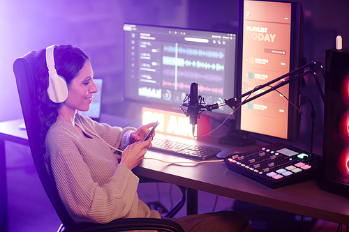 Young adult Caucasian woman wearing casual clothes reading comments in social net on smartphone after finishing live podcast