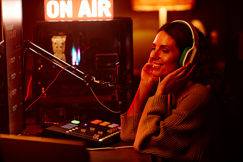 Modern young adult woman working on radio broadcast in amateur home studio at night turning on her favourite music playlist