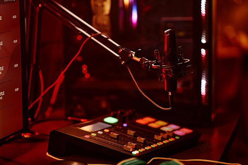 Horizontal no people shot of microphone and small mixing console on table at night, home radio or podcast studio concept