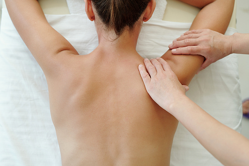 Above shot of back of young woman visiting spa salon where masseur doing her body massage