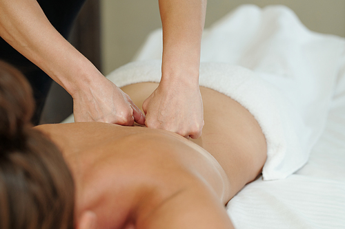 Hands of masseuse pressing punches against back of young relaxed woman during procedure of body massage