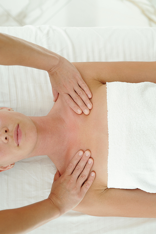 Above angle of young woman having her shoulders massaged by professional masseur of luxurious spa center