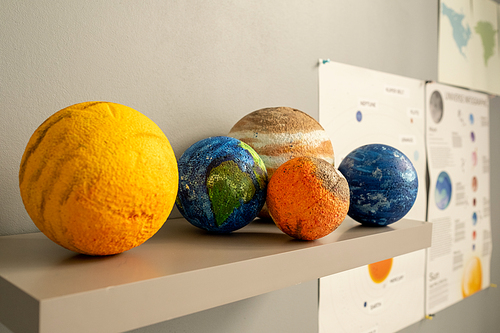 Group of planet models on shelf by white wall inside classroom