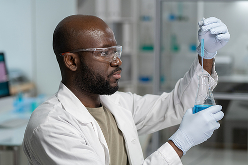 Side view of serious young male scientist in gloves and whitecoat carrying out scientific experiment in modern laboratory