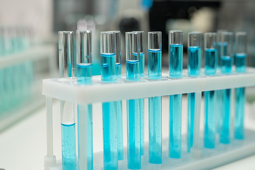 Row of several flasks or test tubes with blue liquid on workplace of modern healthcare worker or scientist in laboratory