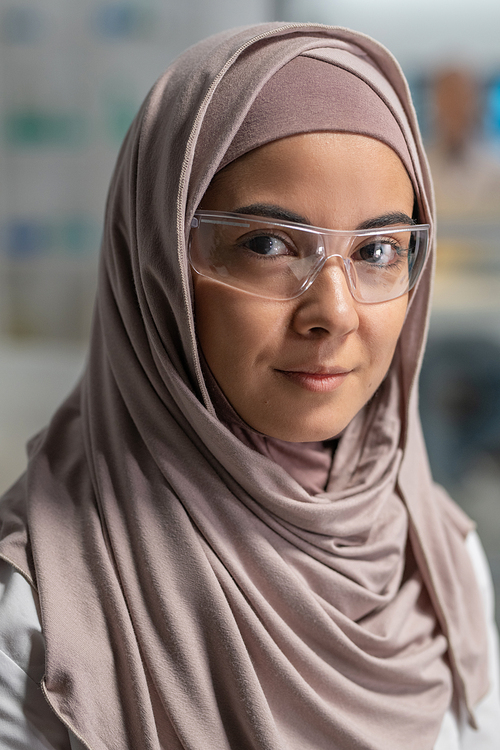 Young successful Muslim female researcher in hijab and protective eyewear standing in front of camera and looking at you