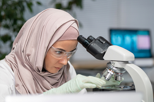 Young Muslim female researcher putting sample of bacteria on small glass while going to study it in microscope in laboratory