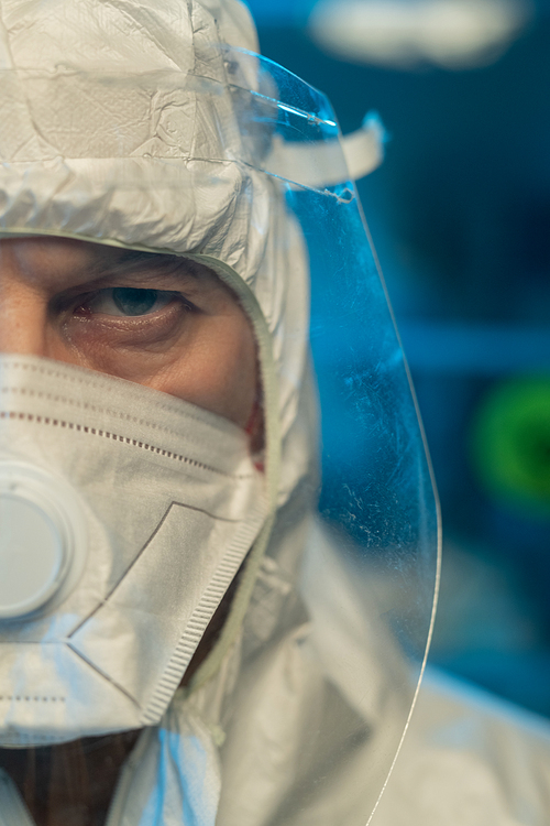 Part of face of male scientist in protective coveralls, respirator and screen standing in front of camera in modern scientific laboratory