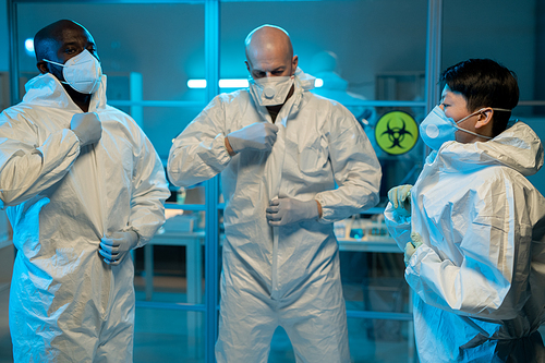 Group of interracial scientists putting on biohazard suits while standing in front of laboratory to work with dangerous substances