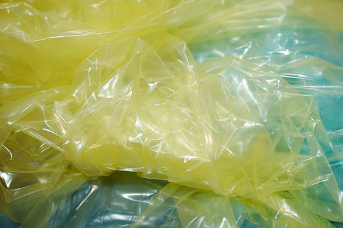 Part of crumpled cellophane of yellow color prepared for wrapping small metallic details of industrial machines over light blue surface