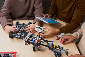 Close-up of students connecting robots with digital tablet at the table during engineering lesson