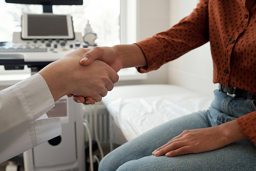 Handshake of young female clinician and patient sitting against ultrasound equipment after medical examination