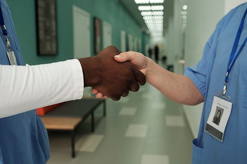 Close-up of mid section of two successful surgeons or general practitioners in blue uniform shaking hands in hospital corridor