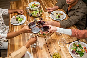 Close-up of people toasting with glasses of red wine while sitting at dining table with meal, they celebrating something at party