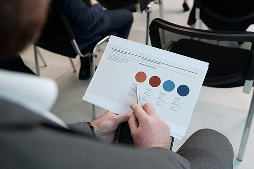 Hands of young businessman pointing at beige circle in financial document while analyzing information during training