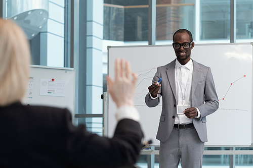 Young smiling African American teacher pointing at female broker raising hand to answer question about presentation at training