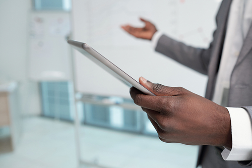 Hand of young African American lecturer holding tablet during presentation of financial information on whiteboard