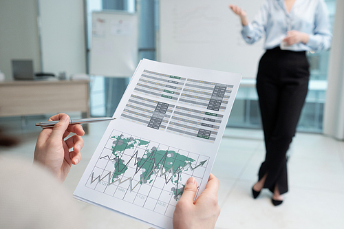 Hands of young female economist pointing at financial document with graphs while sitting in front of coach at conference