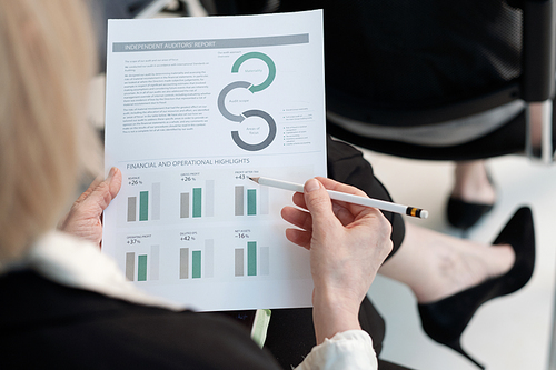 Hand of female economist with pencil pointing at chart in financial document while preparing report about company income