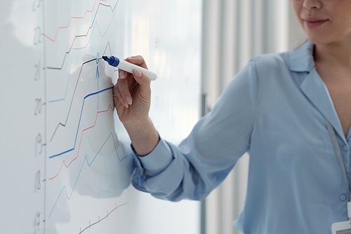 Hand of young female speaker with blue highlighter pointing at graph on whiteboard while explaining audience change of company profit