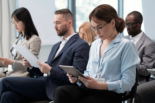 Two rows of contemporary economists in formalwear preparing their reports for conference while looking through documents