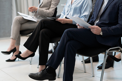 Row of several company employees in formalwear holding documents with financial information while sitting at conference