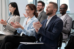 Two rows of happy young intercultural employees clapping hands to speaker after presentation meaning successful report