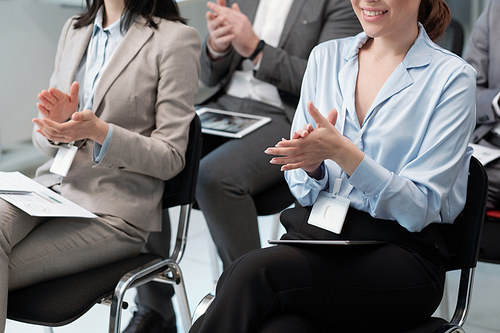 Close-up of two young female brokers in formalwear applauding to speaker at conference after presentation of company profit